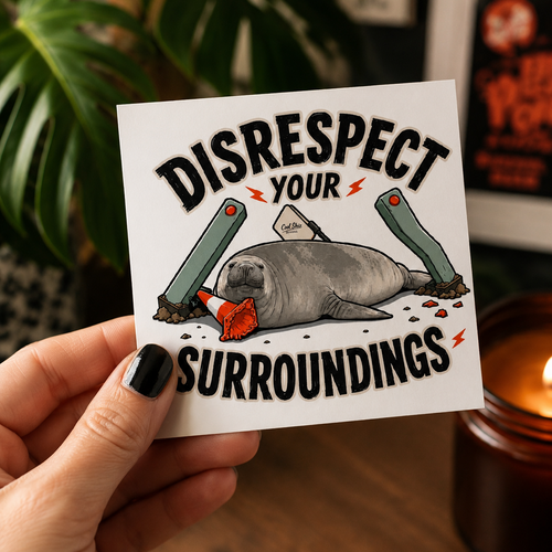A hand holds a Cool Shiz Neil the seal waterproof, scratch resistant, vinyl, 'DISRESPECT YOUR SURROUNDINGS' sticker. The background shows a warm indoor setting with a lit candle, a wooden surface, and blurred green foliage.