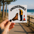 A hand holds a square white Cool Shiz, Neil the seal, Ungovernable, waterproof, scratch resistant, vinyl sticker.